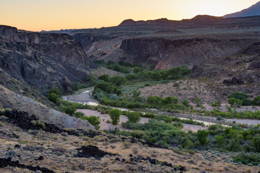 The sun dips below the horizon, creating a fiery orange glow above the Virgin River, near Hurricane, Utah.